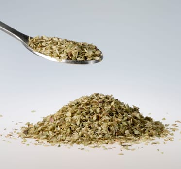 Dried oregano on Tablespoon with a pile beneath it.
