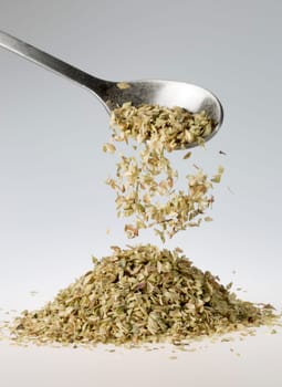 Dried Oregano Falling from Tablespoon onto pile beneath it.