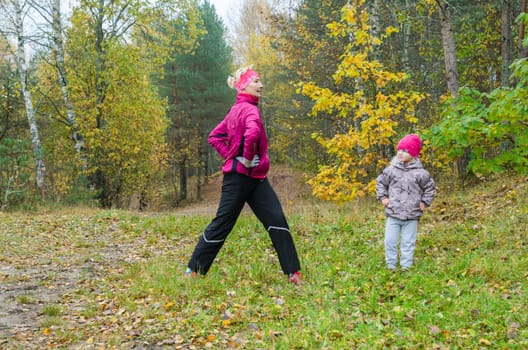 Woman with girl doing aerobics in the autumn park