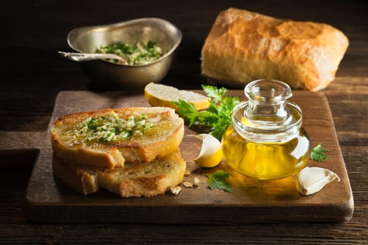 Toasted bread with garlic, herbs and olive oil on wooden background.