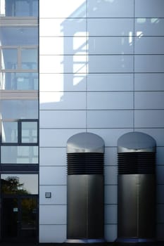 Two large stainless steel ventilation hoods stand next to the entrance of a modern building.
