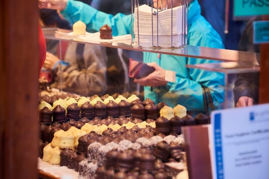 Cropped shot of chocolate covered marshmallow snowballs with consumer paying over the counter in the background.