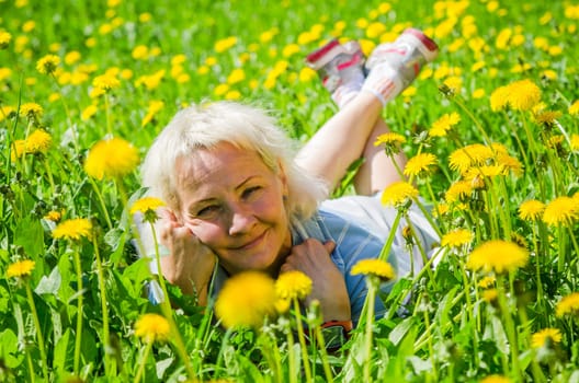 A woman lies in a clearing among the dandelions and sniffs a flower