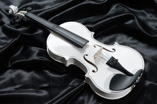 Closeup of a white violin on a background of black satin