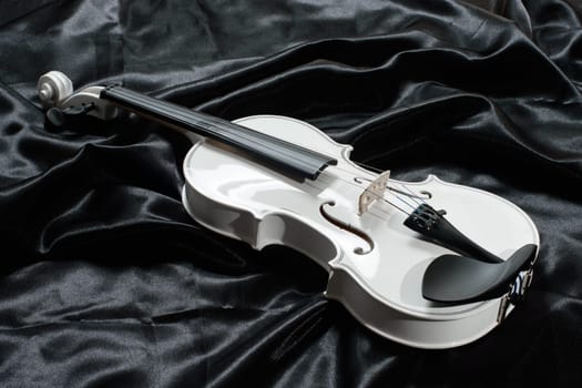 Closeup of a white violin on a background of black satin