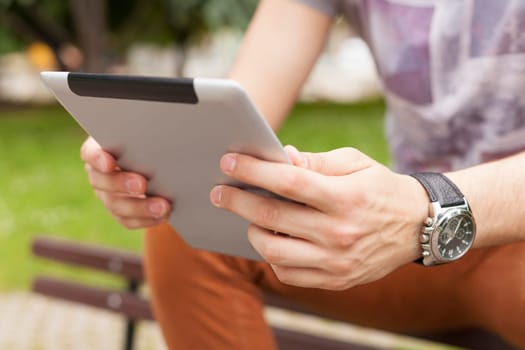 Young man read news and communicate on social networks with tablet computer in park