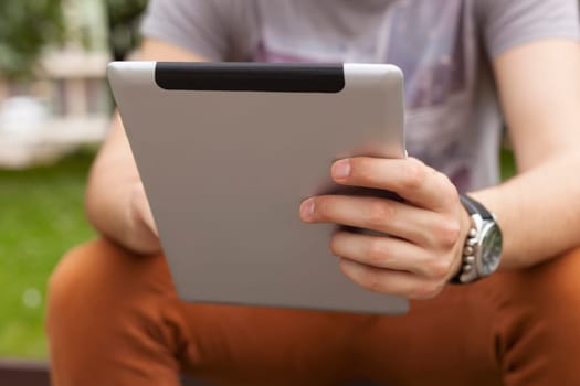 Young man read news and communicate on social networks with tablet computer in park