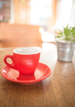 Red cup of coffee and green plant bucket on wooden table, stock photo