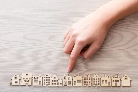 real hand pointing out a house model among the others mini figures in a micro wooden village set