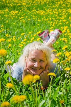 A woman lies in a clearing among the dandelions and sniffs a flower