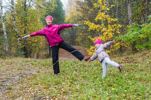 Woman with girl doing aerobics in the autumn park