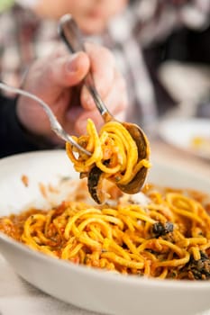 Dinner guest rolling up spaghetti on a fork. Closeup