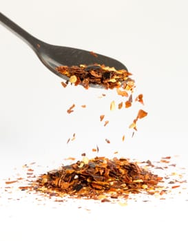 Dried Chili Pepper Falling from Tablespoon into pile of chili pepper on a white background.