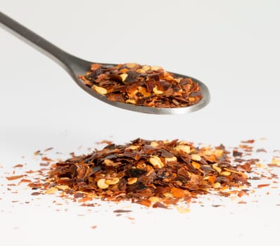 Dried Chili Pepper on Tablespoon with a pile of chili pepper underneath.