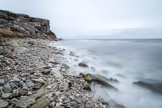 Rocky Shore by Ocean with cliff and a cloudy sky.