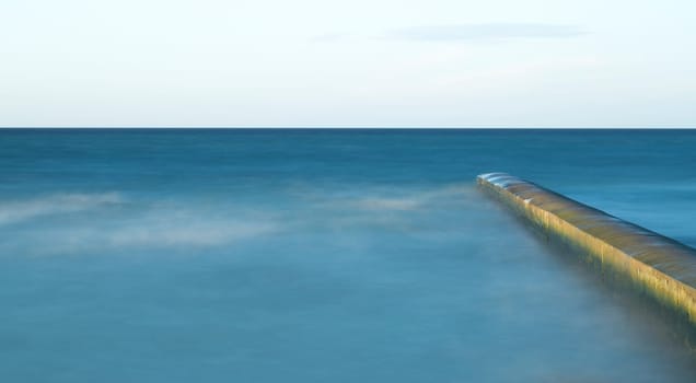 Calm Ocean with Breakwater Structure with clouds in the sky.