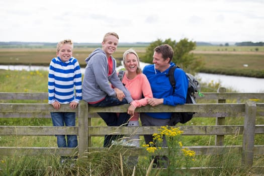 Happy Family of four on a bridge over water in the countryside. They are wearing casual clothing and smiling.