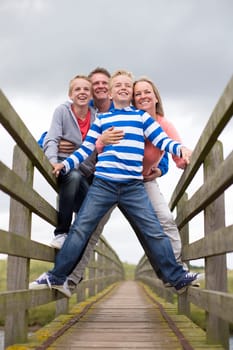 Family Portrait taken at a low angle on a bridge. They are wearing warm casual clothing and smiling.
