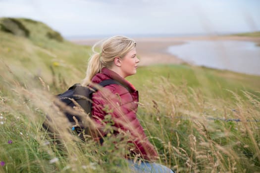 Young woman sitting on a bench in the countryside. She is wearing casual clothing and looking out onto the surroundings.