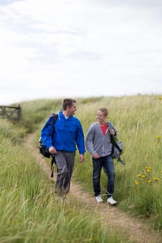 Father and son walking down the sandunes onto the beach. They are wearing warm casual clothing and smiling at each other.