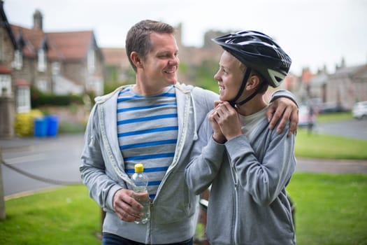 Father and Son getting ready for their bike ride. The father has his arm around his son and they are smiling at each other.