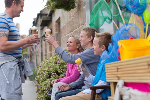 Family enjoying ice cream outside of a shop. They are all holding their cones and smiling.