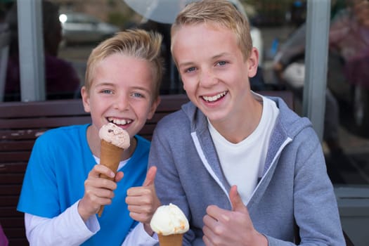 Brothers enjoying ice cream outside of a shop. They are wearing casual clothing and smiling at the camera.