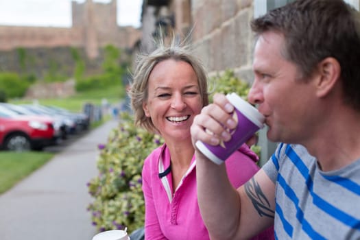 Mature couple laughing as they sit and enjoy a hot drink from a takeaway cup. They are wearing casual clothing and look very happy.