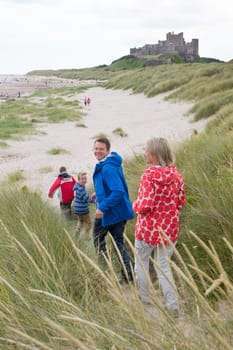Family of four running down the sandunes onto the beach. A castle can be seen in the background.