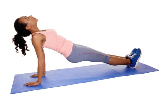 A young African American girl lying on a yoga mat, doing exercises, in blue.tights, isolated for white background..