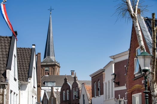 Typical Dutch village center with the steeple of the church always visible. In the left corner a Dutch flag banner. The picturesque Dorpsstraat  or Village Street is the main street of the village Ouderkerk aan den IJssel in the Netherlands. The river IJssel is just behind the houses on the left side.
