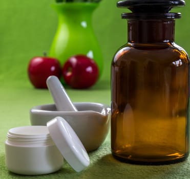 A pharmacist's bottle,an open cream can and a mortar against a green background