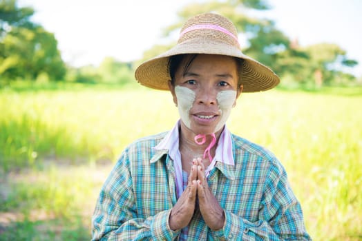 Portrait of a mature Burmese female farmer with thanaka powdered face in blessing gesture.