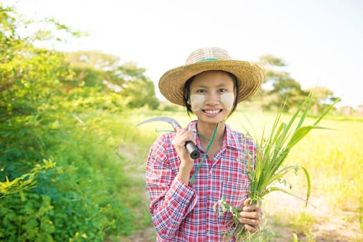 Portrait of a young Burmese female farmer with thanaka powdered face working in field.