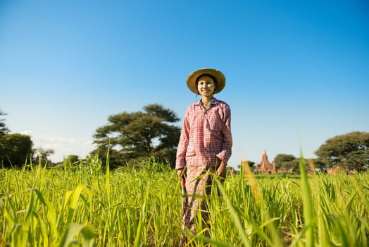 Portrait of a young Asian Myanmar farmer with thanaka powdered face standing in the farm field.