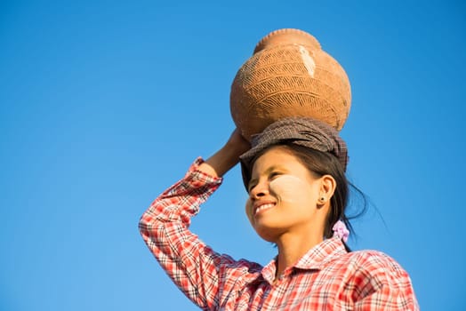 Portrait of Young Asian Burmese traditional female farmer carrying clay pot on head going back home, Bagan, Myanmar