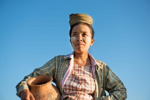 Portrait of mature Asian Burmese traditional female farmer carrying clay pot, Bagan, Myanmar