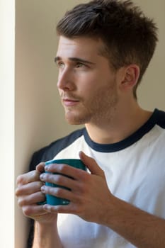 Portrait of a man looking out a window with a hot drink in his hands.