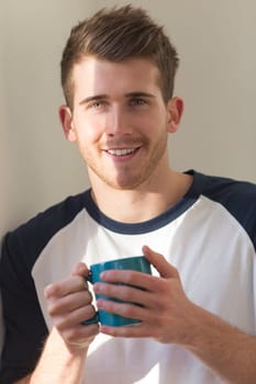 Portrait of a man holding a hot drink. He is smiling at the camera.