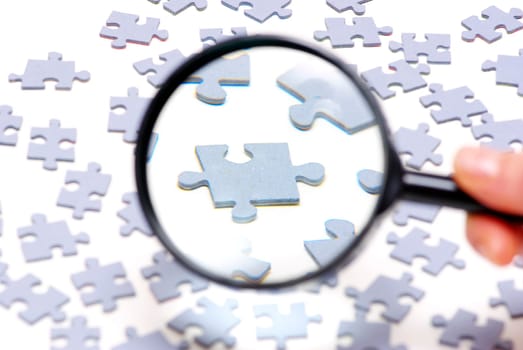 Hand with magnifying glass and puzzle isolated on white background