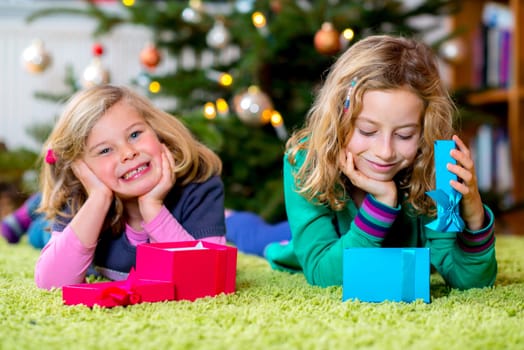 two blond girls with presents in front of christmas tree