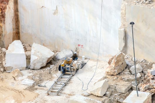Industrial marble quarry, with cut blocks and workers and machines bulldozer at work.