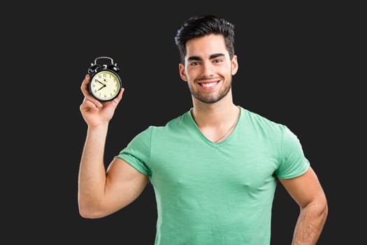 Portrait of handsome young man holding a clock, isolated on gray background