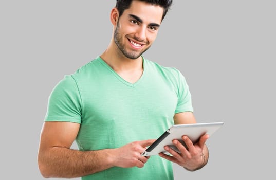 Handsome young man showing something on a tablet, isolated over gray background