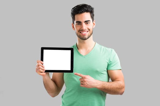 Handsome young man showing something on a tablet, isolated over gray background