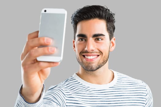Handsome young man making a selfie picture with phone, isolated over gray background