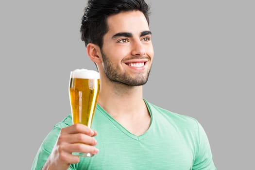Portrait of handsome young man tasting a draft beer, isolated on gray background