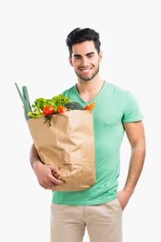 Handsome young man carrying a bag full of vegetables, isolated over gray background