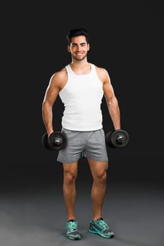 Portrait of handsome young man lifting weights, isolated over a gray background