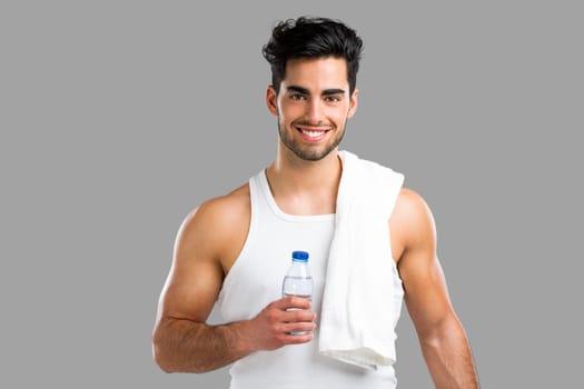 Portrait of a athletic young man holding a water bottle, isolated over a gray background